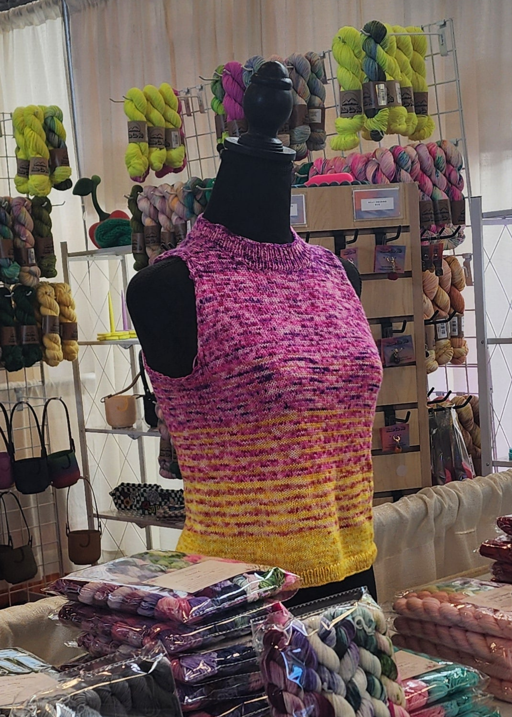 Mannequin wearing a colorful knitted tank top in a store setting with yarn and fabric displays.